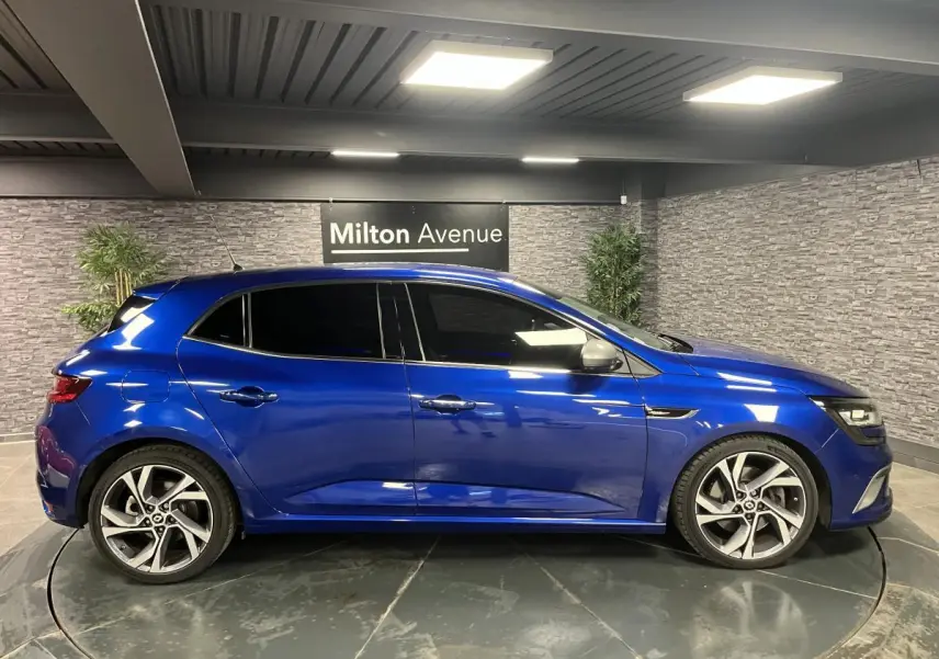 Profil droit d’une Renault Mégane GT bleu Iron 2016 avec jantes alliage 18 pouces et vitres surteintées.