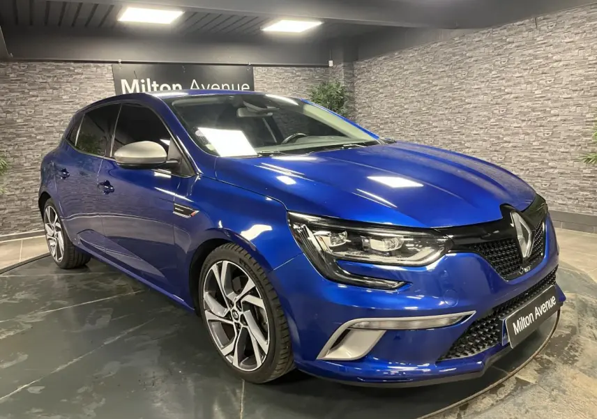 Renault Mégane GT bleu Iron en 3/4 avant droit, avec jantes alliage 18 pouces et calandre noire nid d'abeilles.