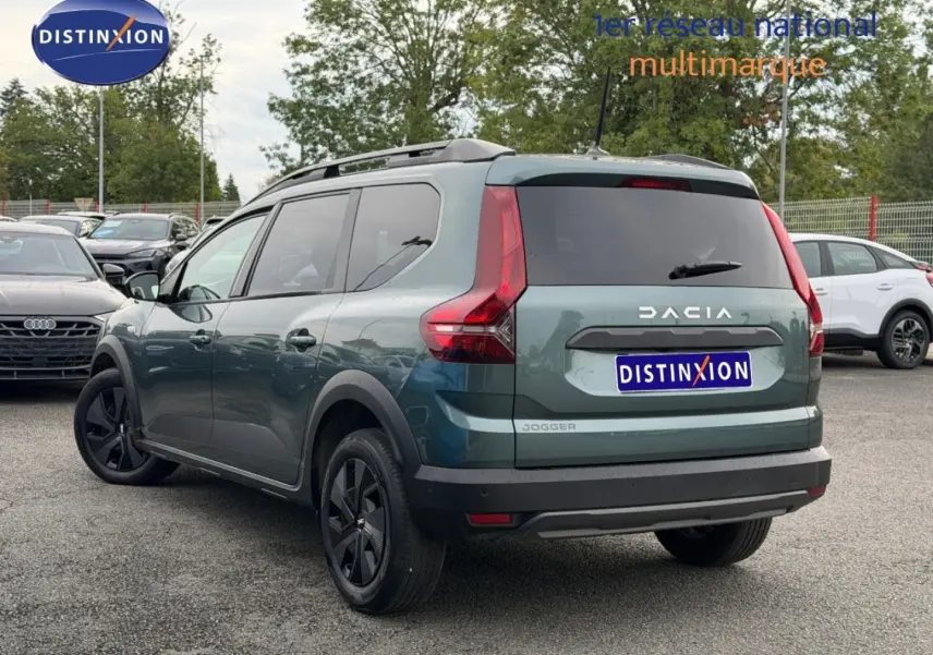 Vue 3/4 arrière droite d'un Dacia Jogger 2025 vert cèdre métallisé avec barres de toit et vitres arrière surteintées.