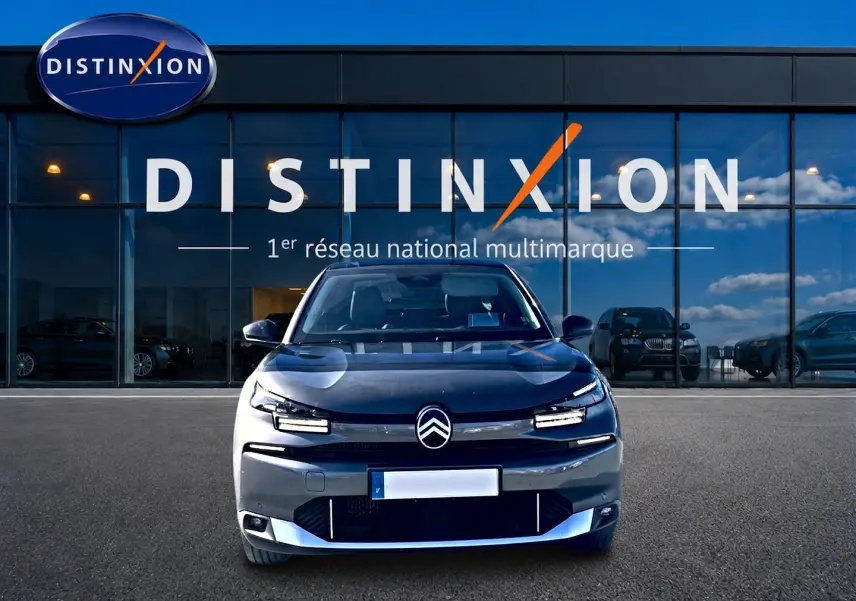 Vue frontale d'une Citroën C4 X gris mercure devant une vitrine avec logo Distinxion en arrière-plan.