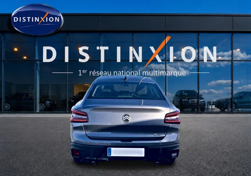 Vue arrière d'une Citroën C4 X gris mercure garée devant une vitrine avec logo Distinxion en arrière-plan.