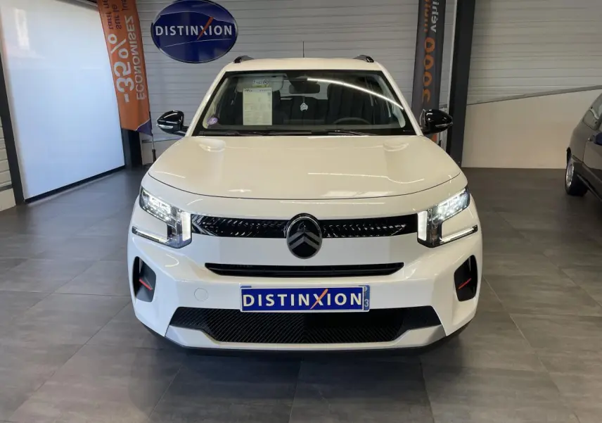 Vue frontale d'une Citroën C3 blanche avec calandre noire brillante et projecteurs LED allumés en showroom.