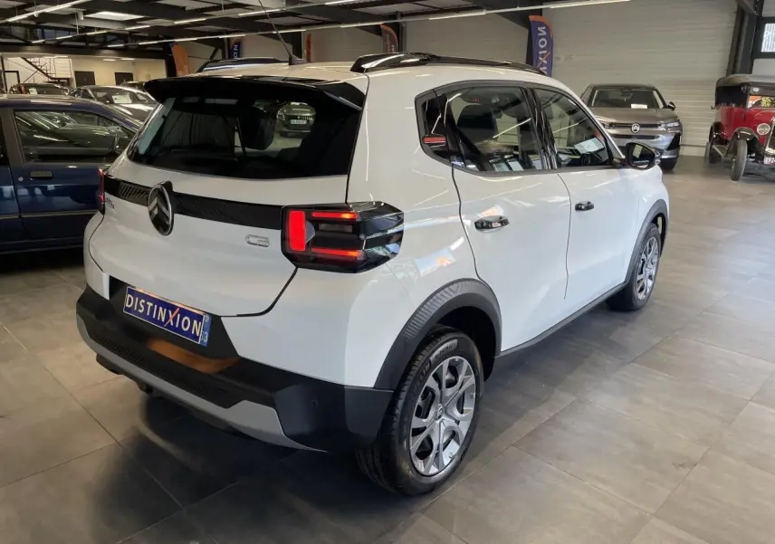 Vue 3/4 arrière droite d'une Citroën C3 blanche avec barres de toit noires et feux arrière LED distinctifs.