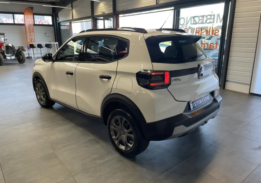 Vue 3/4 arrière droite d'une Citroën C3 blanche avec toit noir et jantes 17 pouces en intérieur showroom.