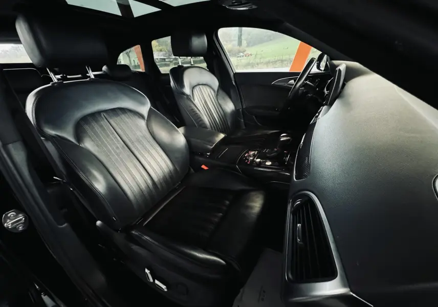 Vue intérieure côté conducteur de l'Audi A6 Avant Allroad noire, sièges cuir noir et tableau de bord moderne.