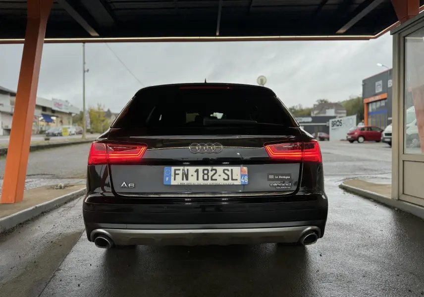 Vue arrière d'une Audi A6 Avant Allroad noire avec feux arrière allumés, sous un abri couvert.