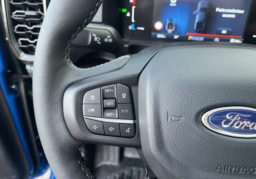 Gros plan sur le volant cuir multifonctions du Ford Ranger 2025 bleu lightning, avec commandes intégrées et tableau de bord numérique visible.