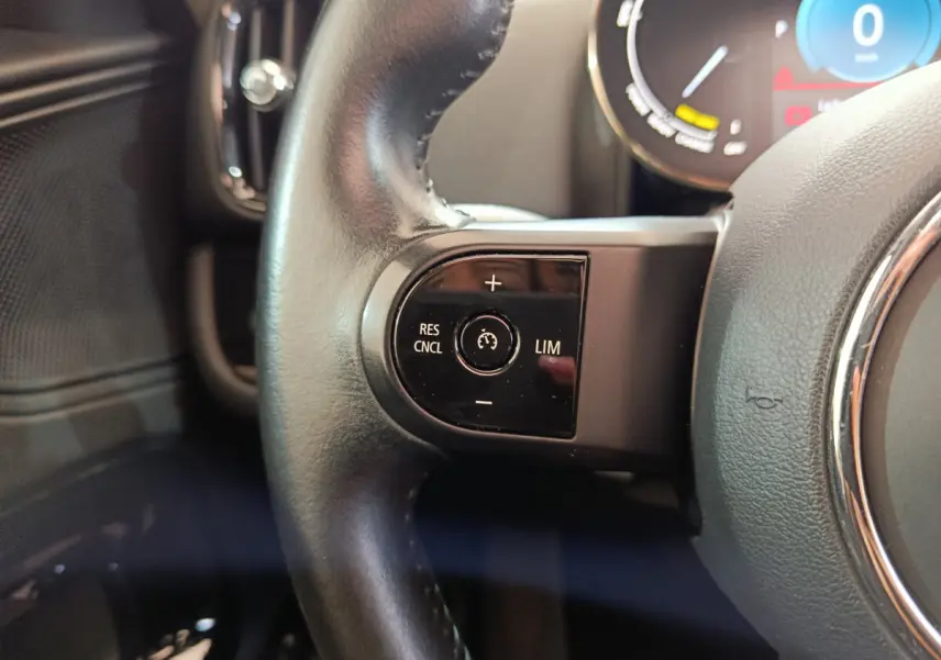 Gros plan sur la commande de régulateur de vitesse au volant cuir du MINI Countryman blanc hybride rechargeable.