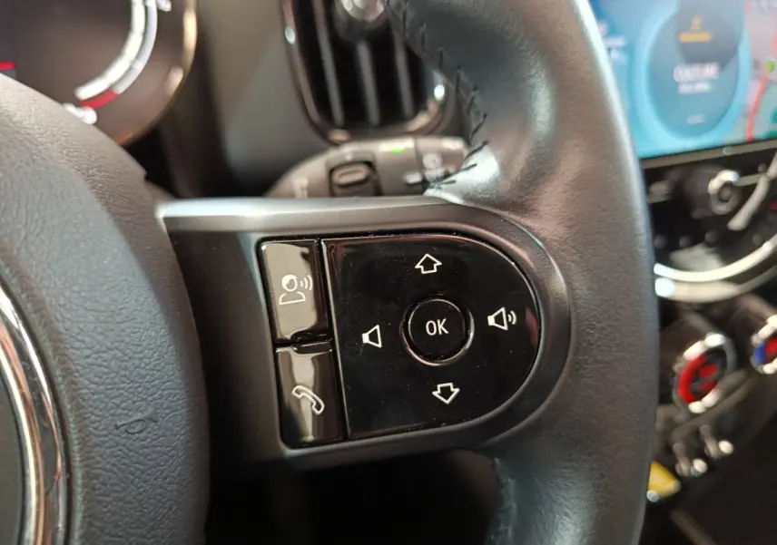 Gros plan sur les commandes noires du volant cuir du MINI Countryman blanc, avec tableau de bord et écran tactile en arrière-plan.