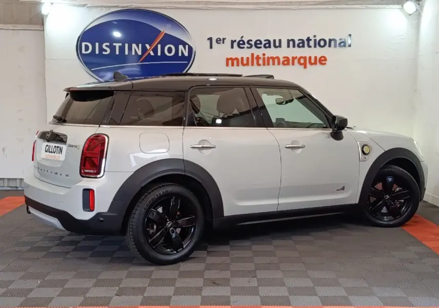 Vue de profil côté gauche d'un MINI Countryman blanc avec toit noir et jantes noires dans un showroom.