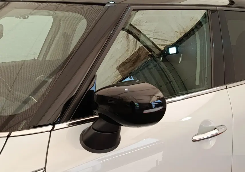 Rétroviseur noir en gros plan côté gauche sur MINI Countryman blanc, avec porte et vitre avant visibles.