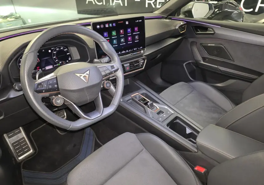 Intérieur avant de la CUPRA Leon 2024, vue côté conducteur, tableau de bord noir avec écran tactile et volant multifonction.