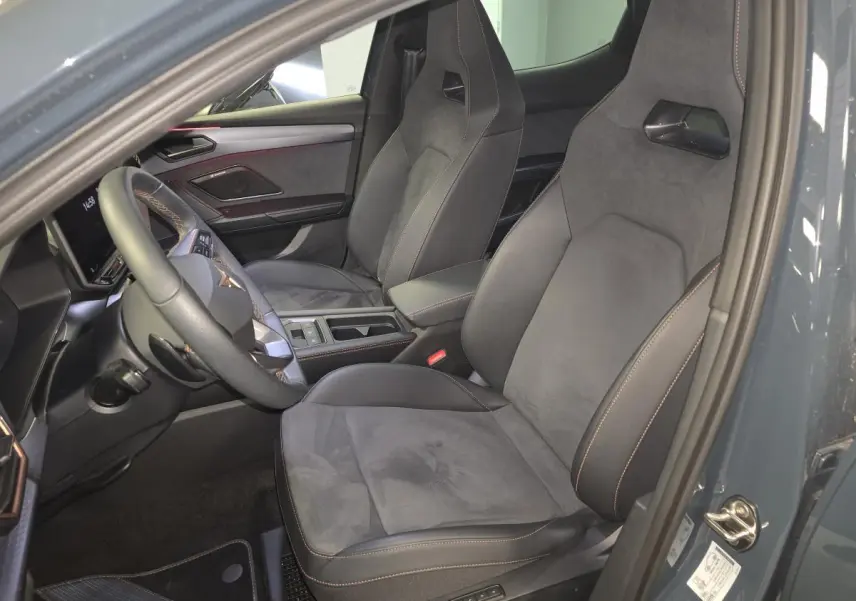 Vue intérieure côté conducteur de la CUPRA Leon 1.5 e-Hybrid 2024 avec sièges baquets suédine noirs et surpiqûres cuivrées.