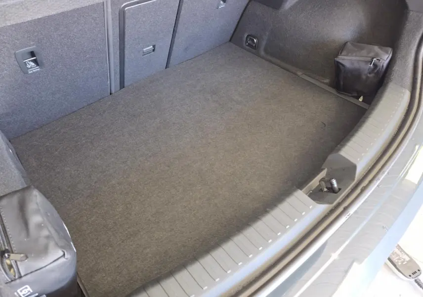 Coffre spacieux vu de dessus de la CUPRA Leon 1.5 e-Hybrid bleu, avec tapis gris et petits rangements latéraux.