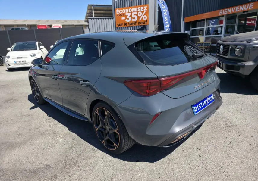 Vue 3/4 arrière droite d'une CUPRA Leon hybride rechargeable bleu Fjord avec jantes alliage 19'' cuivrées et bandeau lumineux arrière.