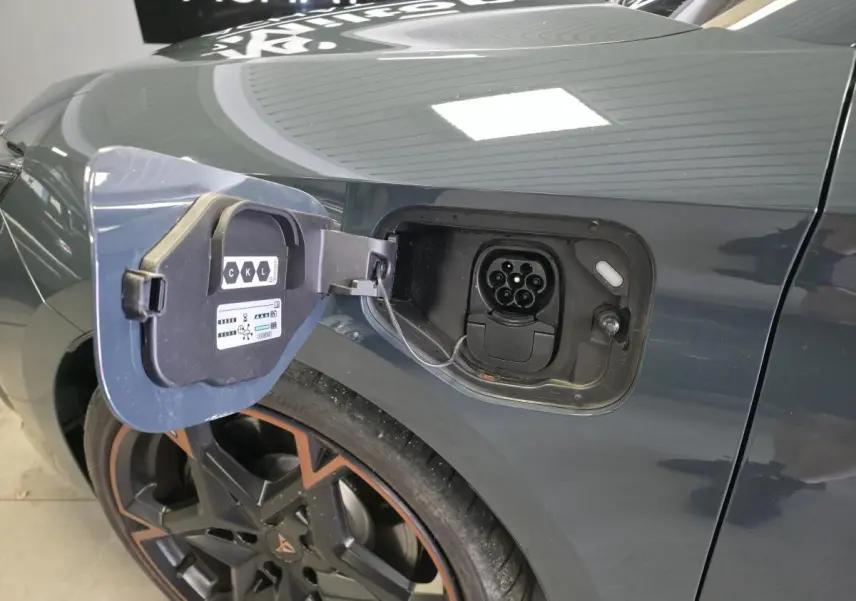 Prise de recharge ouverte côté arrière gauche sur CUPRA Leon bleu avec jante alliage 19'' cuivrée visible.
