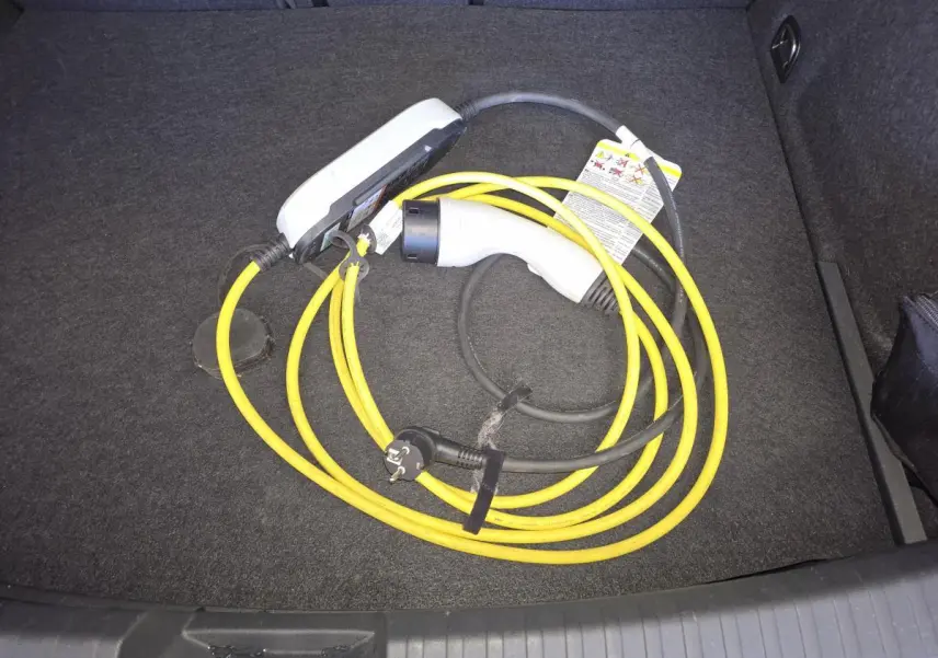 Câble de recharge hybride jaune et blanc dans le coffre d'une CUPRA Leon bleu 2024.