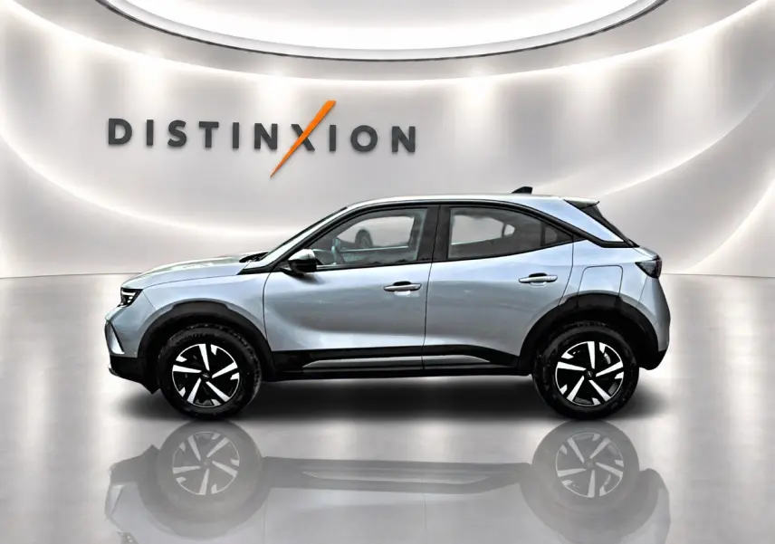 Opel Mokka gris en profil droit dans un showroom lumineux avec jantes noires et logo Distinxion en arrière-plan.