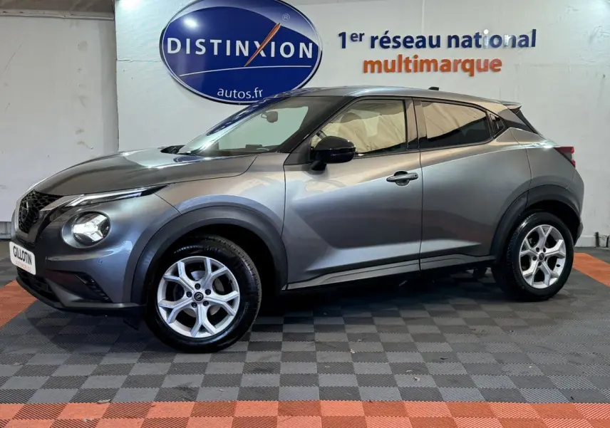 Profil droit d'un Nissan Juke gris clair 2021 dans un showroom avec logo Distinxion en arrière-plan.