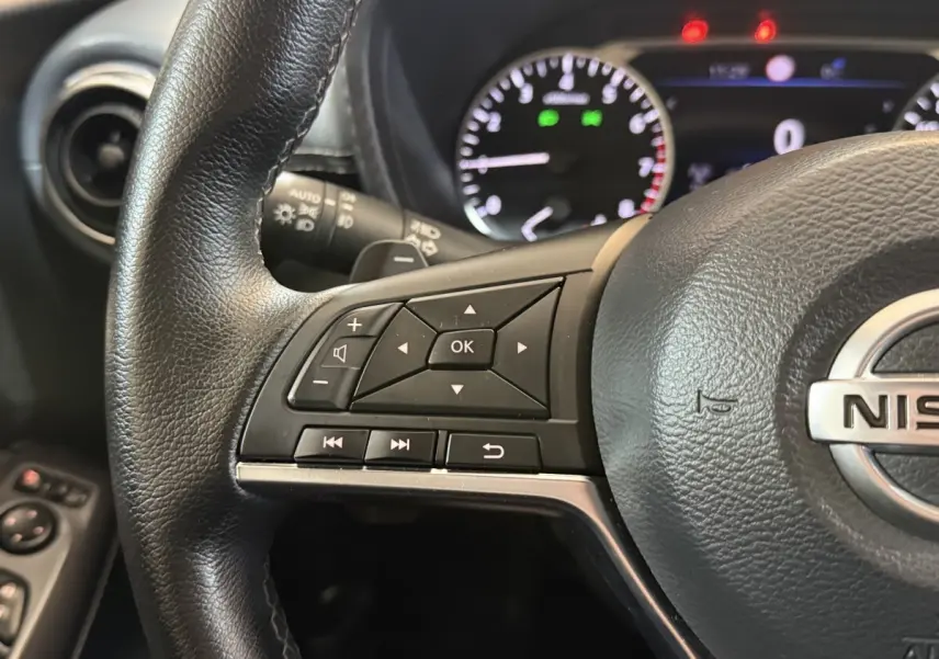 Gros plan sur le volant cuir noir du Nissan Juke 2021, avec commandes multifonctions et tableau de bord éclairé en arrière-plan.
