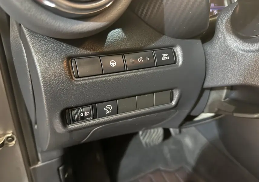 Gros plan sur les commandes côté gauche du tableau de bord gris du Nissan Juke Tekna 2021, avec réglages éclairage et régulateur.