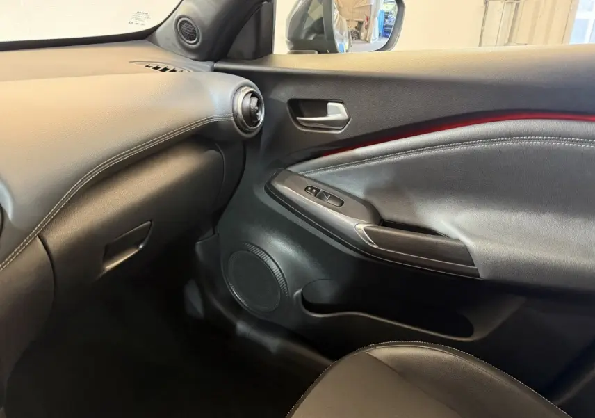 Intérieur côté passager du Nissan Juke Tekna 2021, montrant la porte noire avec bande rouge et tableau de bord gris clair.