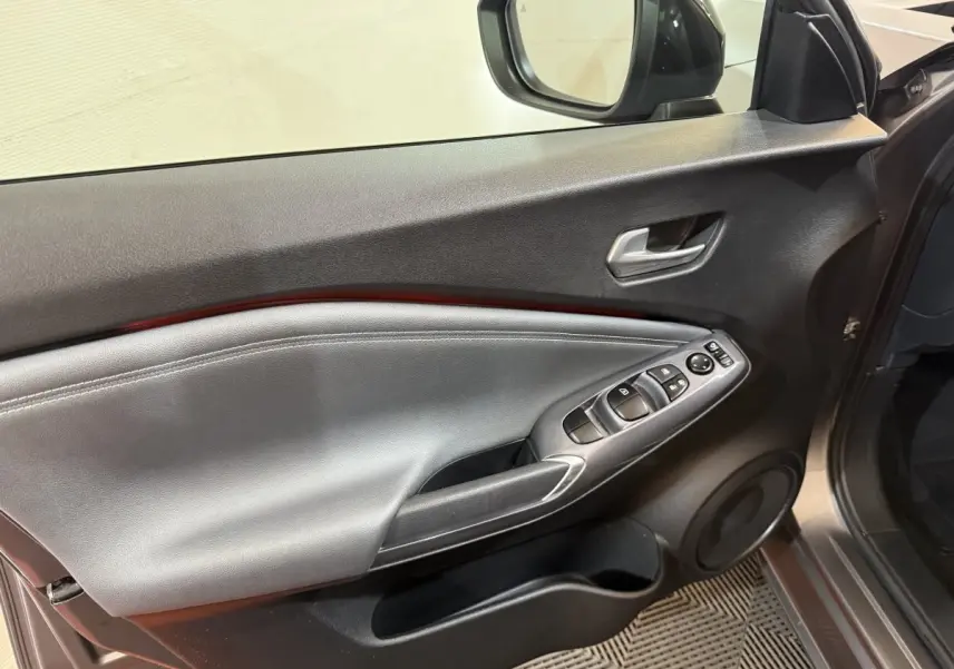 Vue intérieure du panneau de porte côté conducteur du Nissan Juke gris clair, avec commandes électriques et poignée argentée.