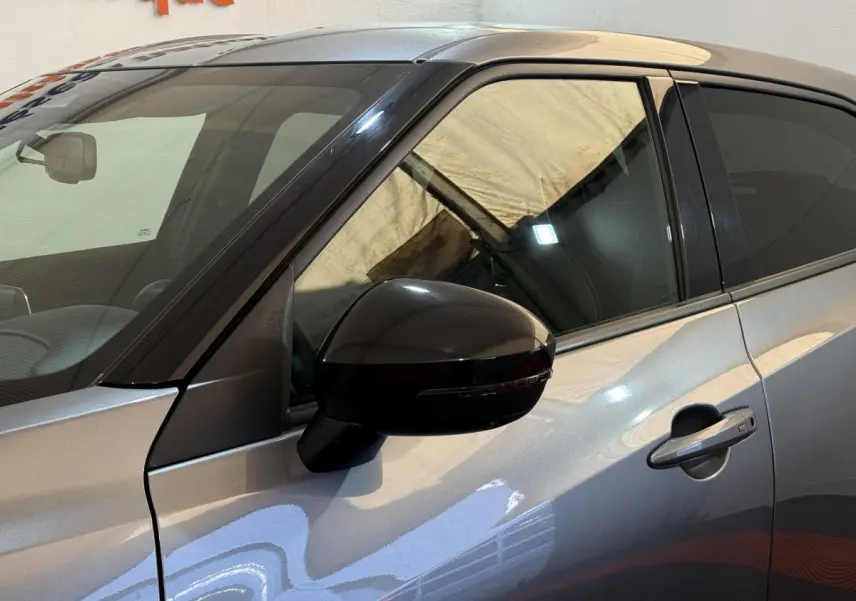 Vue côté gauche rapprochée du Nissan Juke gris clair 2021, mettant en valeur la portière et le rétroviseur noir brillant.