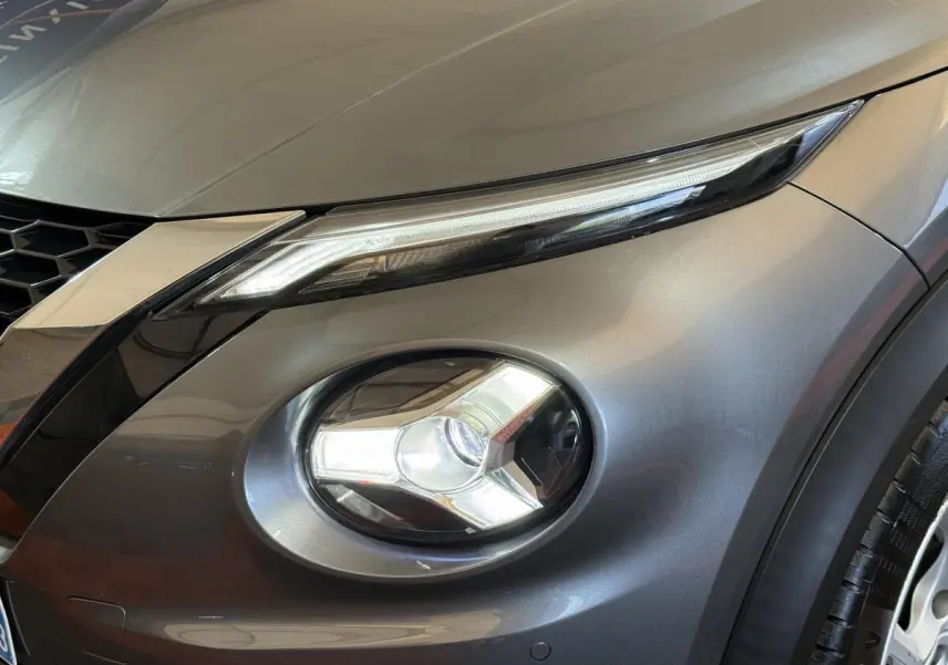 Gros plan sur le phare avant droit et la calandre d'un Nissan Juke gris clair 2021, finition Tekna.