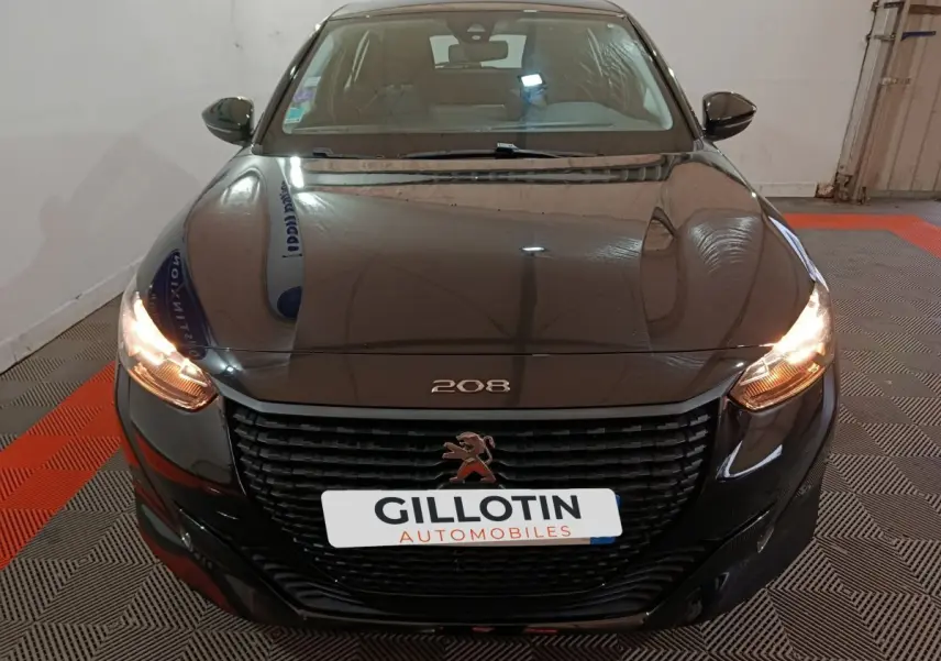 Vue avant d'une Peugeot 208 noire de 2022 avec phares allumés et calandre noire distinctive.