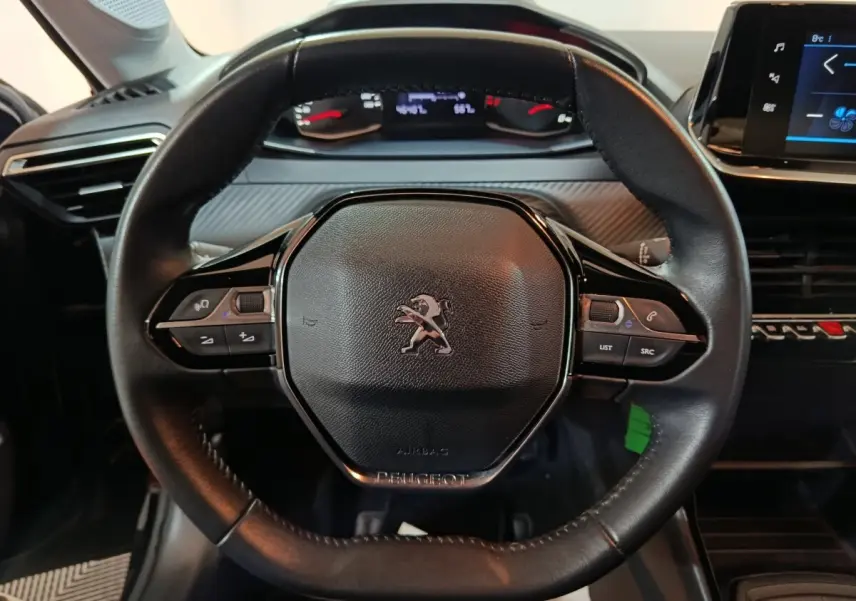 Vue rapprochée du volant noir de la Peugeot 208 2022 avec commandes intégrées et tableau de bord numérique en arrière-plan.
