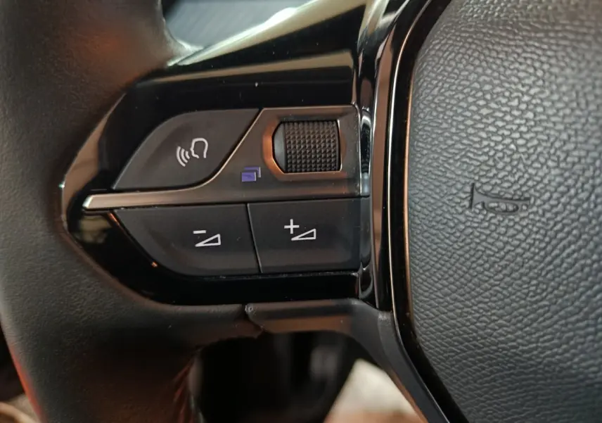 Gros plan sur les commandes gauche du volant noir de la Peugeot 208 2022, avec boutons de volume et reconnaissance vocale.