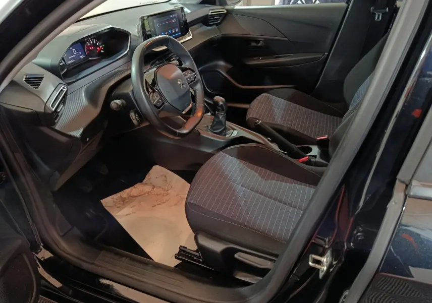 Intérieur avant droit de la Peugeot 208 noire 2022, volant compact, tableau de bord numérique et sièges tissu gris.