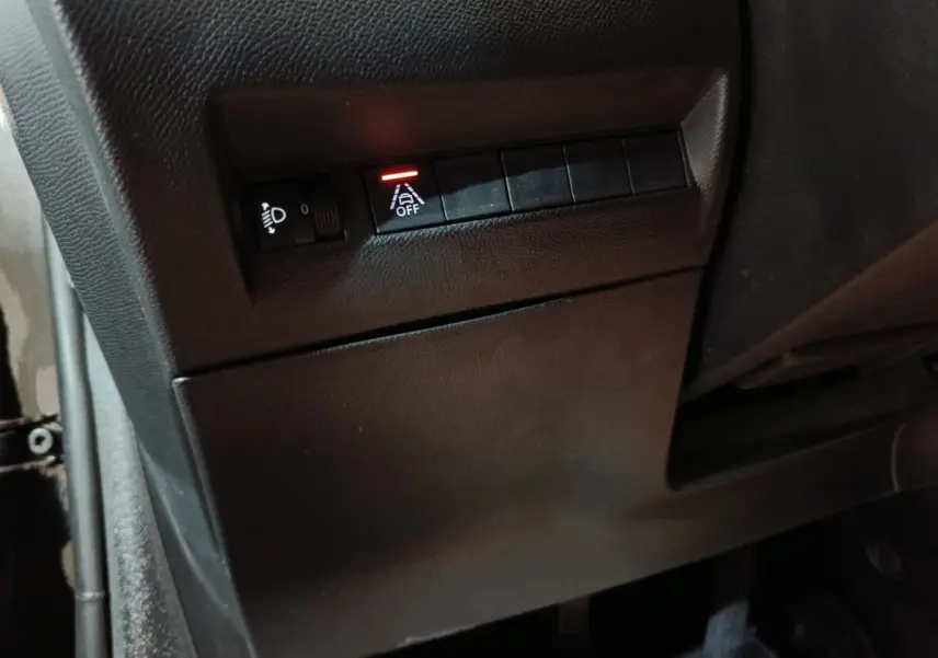 Détail intérieur côté gauche de la Peugeot 208 noire 2022 montrant les commandes de réglage des phares et d'assistance à la conduite.