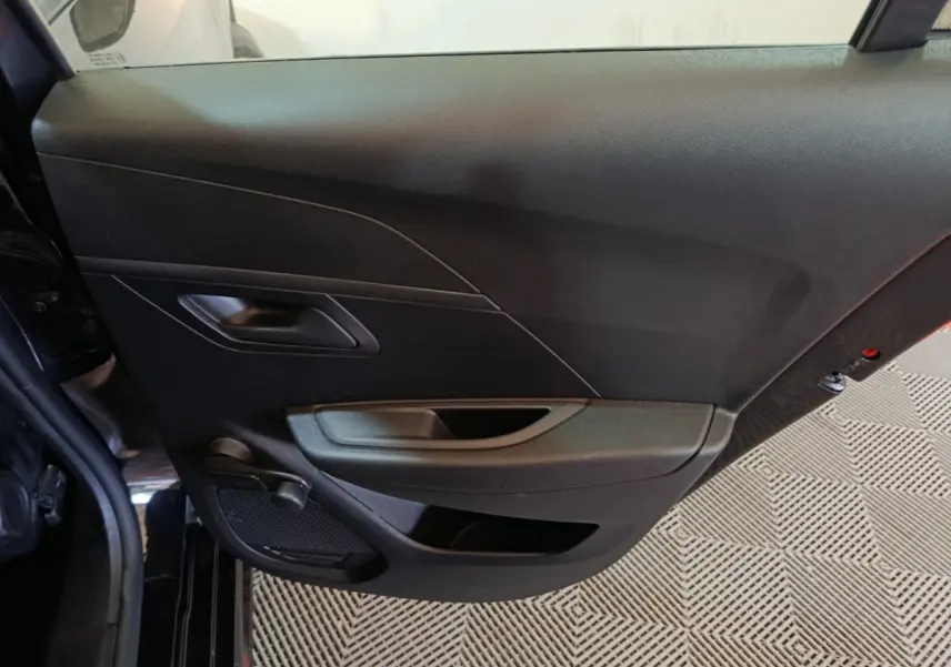 Vue intérieure de la porte arrière gauche noire d’une Peugeot 208 1.2 PT 75 S&S Premium 2022 avec poignée et haut-parleur intégrés.