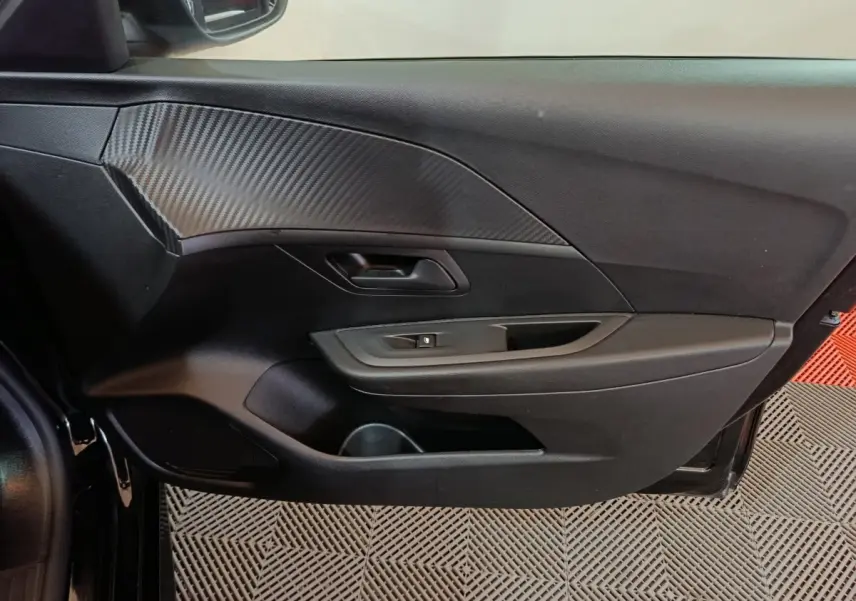 Vue intérieure côté gauche de la porte avant d'une Peugeot 208 noire avec insert décoratif effet carbone.