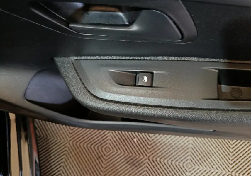 Gros plan sur la commande de lève-vitre côté conducteur de la Peugeot 208 noire, intérieur en plastique noir.