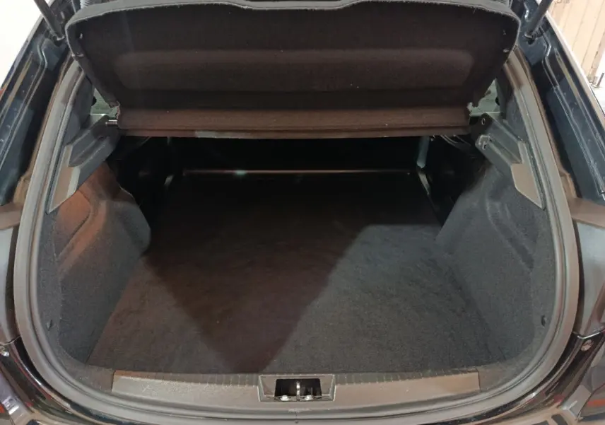 Coffre ouvert vu de l'arrière d'une Peugeot 208 noire, montrant un espace de chargement vide et propre.