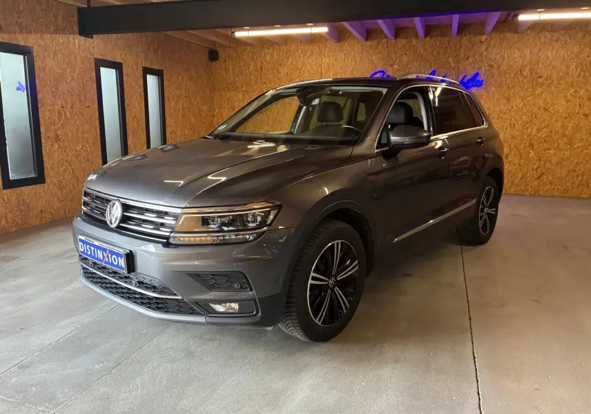 Volkswagen Tiguan gris 3/4 avant droit, avec jantes noires et détails chromés, en intérieur sur sol béton.