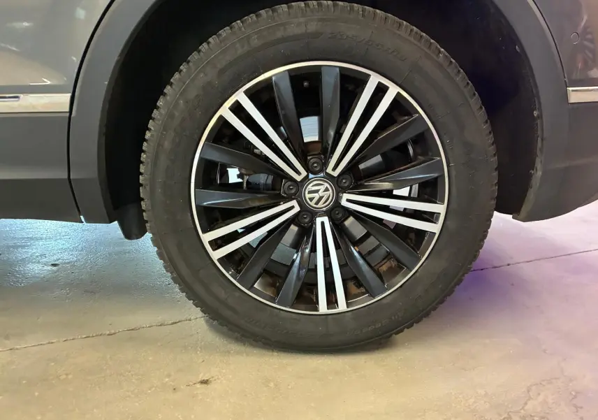 Gros plan sur la roue avant droite d'un Volkswagen Tiguan gris, mettant en valeur la jante alliage noire et argentée.