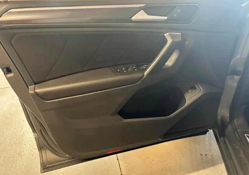 Vue intérieure côté gauche de la porte avant d’un Volkswagen Tiguan gris, avec commandes électriques et garniture noire.