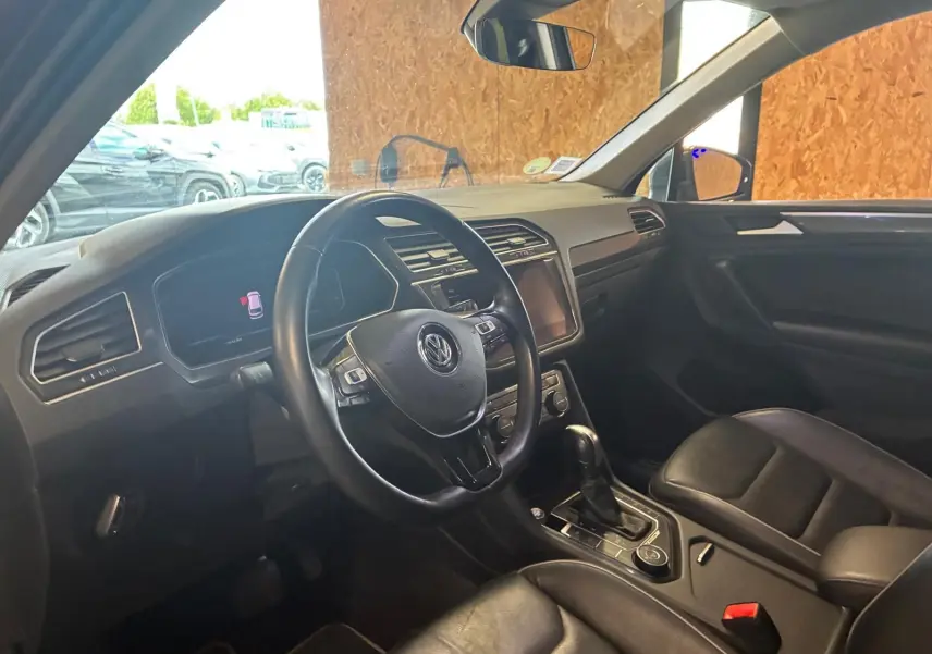 Vue intérieure côté conducteur du Volkswagen Tiguan gris 2020, avec volant cuir et console centrale équipée.