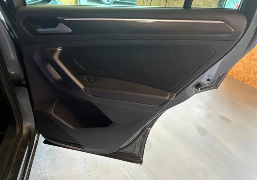 Vue intérieure de la porte arrière gauche gris foncé du Volkswagen Tiguan 2020 avec poignée et commande de fenêtre intégrées.
