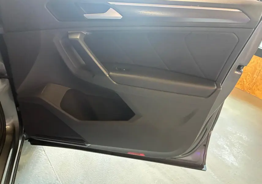 Vue intérieure du panneau de porte côté gauche du Volkswagen Tiguan gris, avec garniture noire et poignée intégrée.
