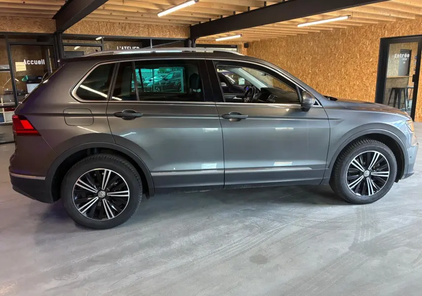 Vue de profil côté gauche d'un Volkswagen Tiguan gris 2020 garé en intérieur avec jantes alliage noires et chrome.