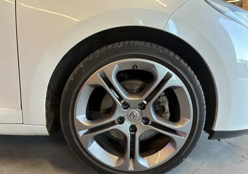 Gros plan sur la roue avant gauche argentée d’une Renault Mégane Coupé blanche, montrant la jante et le pneu.
