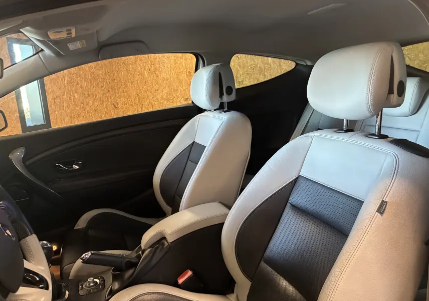 Vue intérieure côté gauche de la Renault Mégane Coupé 2.0 DCI 165 GT 2014 avec sièges cuir bicolores noir et blanc.