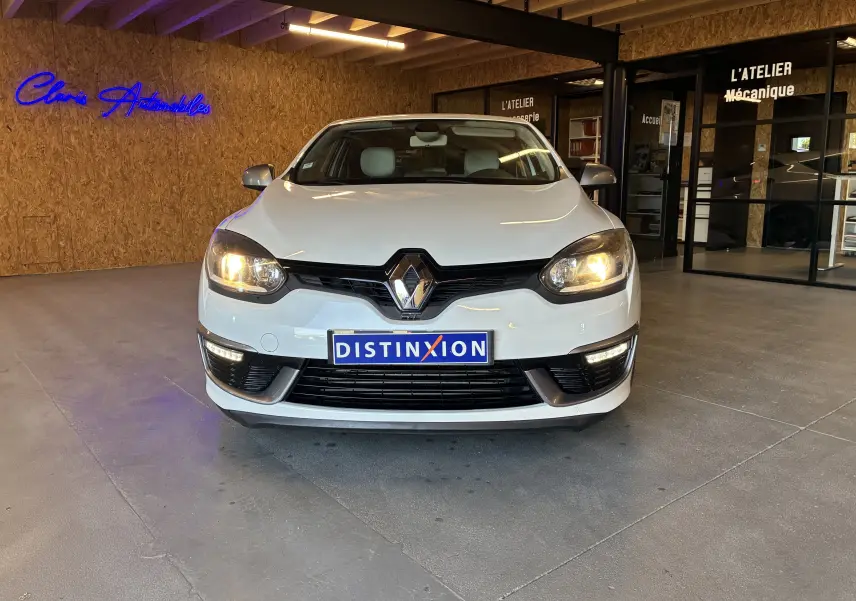 Renault Mégane Coupé blanc vue de face en intérieur, phares allumés et calandre noire distinctive.