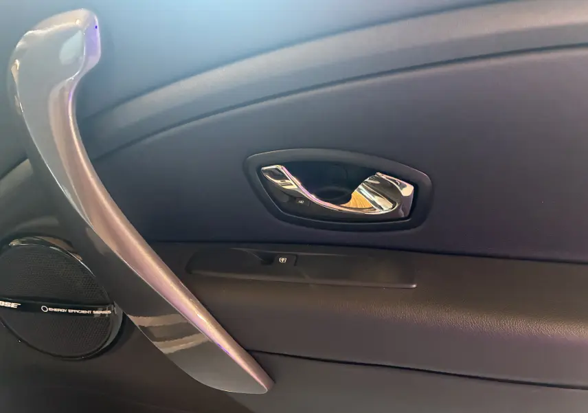Gros plan de la poignée intérieure côté droit en chrome et plastique noir de la Renault Mégane Coupé 2.0 DCI 165 GT blanche.