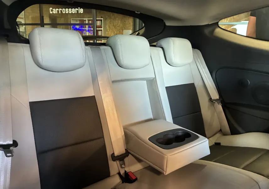 Vue intérieure arrière de la Renault Mégane Coupé 2014, sièges bi-ton gris clair et noir avec accoudoir central rabattable.
